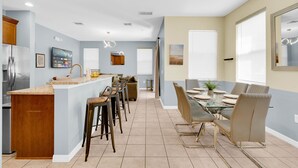 Een moderne keuken met een centraal eiland, barkrukken, een eettafel met stoelen en een grote spiegel.