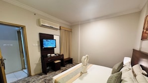 A hotel room with a bed, a desk with a flat-screen TV, an air conditioner, and a door leading to another room. - alryada grand (Makkah)