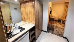 A hotel room with a wooden wardrobe, a vanity with a mirror, a small table with toiletries, and a chair in the corner. - alryada grand (Makkah)
