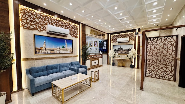 A modern lobby with a blue sofa, a reception desk, and a decorative wall with geometric patterns. - alryada grand (Makkah)