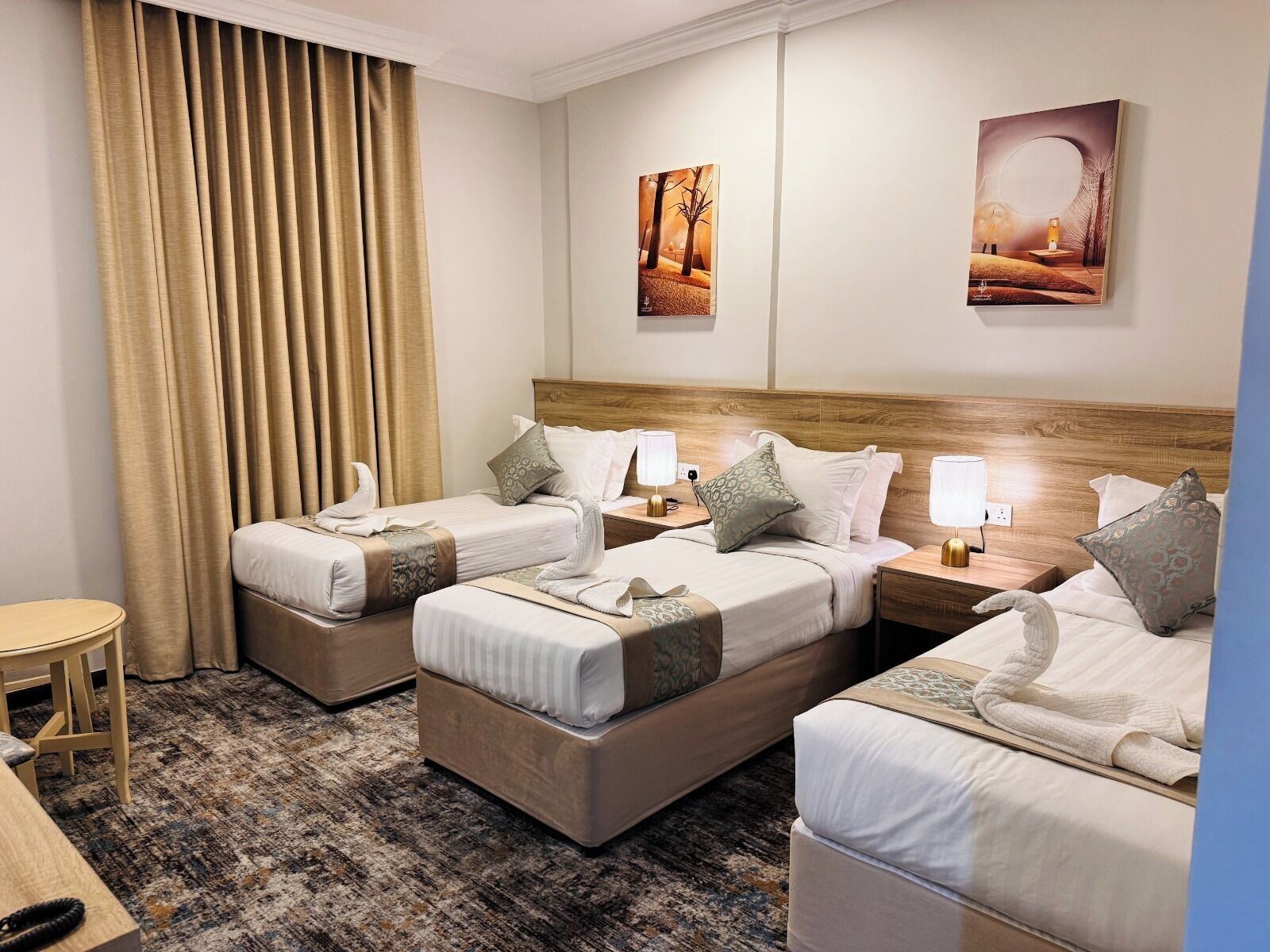 Habitación de hotel con dos camas, una mesita pequeña y un ventanal grande con cortinas.