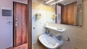Ein modernes Badezimmer mit Holztür, Waschbecken in Weiß, Spiegel und Handtuchhalter.
