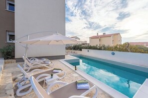 Una piscina en la azotea con sillas de descanso y sombrillas, rodeada de edificios.