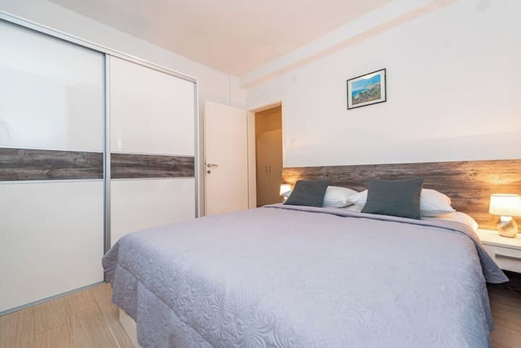 A bedroom with a bed, a nightstand, a lamp, a wardrobe, and a door.