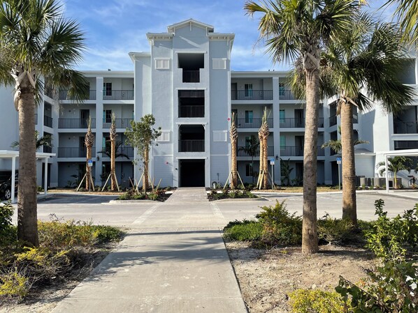 A multi-story building with a central entrance, surrounded by palm trees and a paved walkway. -  Bright spacious 2 bedroom 2 bath condo In Heritage Landing a gated community (Punta Gorda)