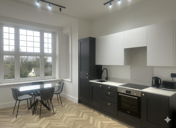 Una cocina moderna con un ventanal grande, muebles oscuros y un suelo con patrón de espiga.