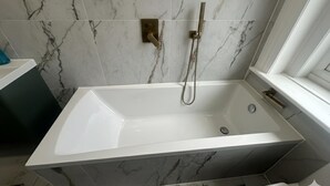 Een moderne badkamer met een vrijstaand bad, een handdouche en een betegelde wand van marmer.