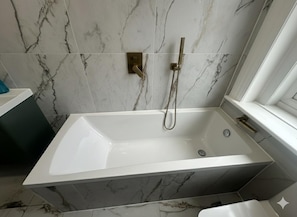 A modern bathroom with a freestanding bathtub, a handheld showerhead, and a marble-tiled wall.