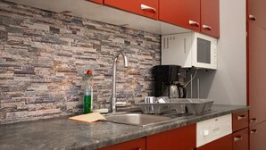 Eine Küche mit Steinrückwand, Spüle aus Edelstahl, Mikrowelle und roten Schränken.