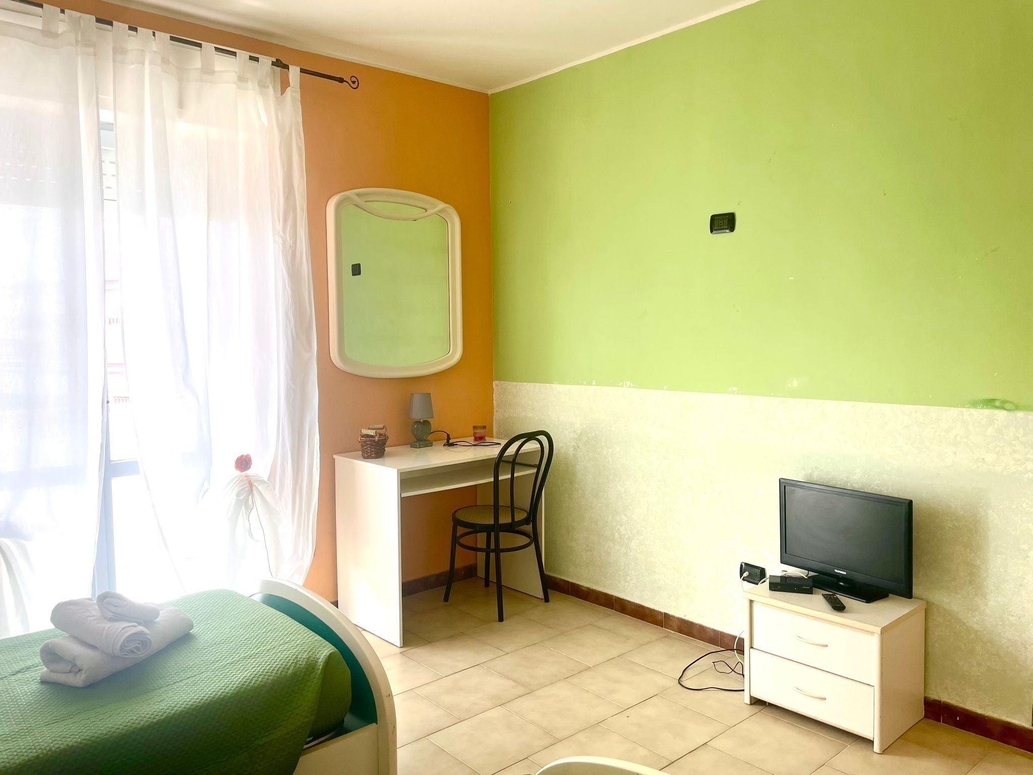 A room with a bed, a desk, a chair, a television, and a window with curtains.