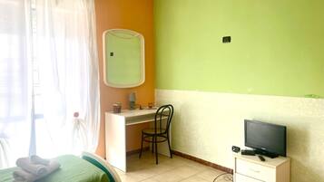 A room with a bed, a desk, a chair, a television, and a window with curtains.