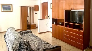 Ein Wohnzimmer mit einer Couch, Holzsäcken, einem Fernseher und einer Tür zu einem weiteren Raum.
