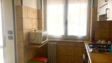 Eine Küche mit einer Mikrowelle auf einem Regal, einem Fenster mit Vorhängen, einem Herd und gefliesten Wänden.