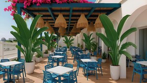 An outdoor patio area with blue tables and chairs, surrounded by large potted plants and a pergola with hanging lamps. - Urania Arenal by Soho Boutique (Llucmajor)