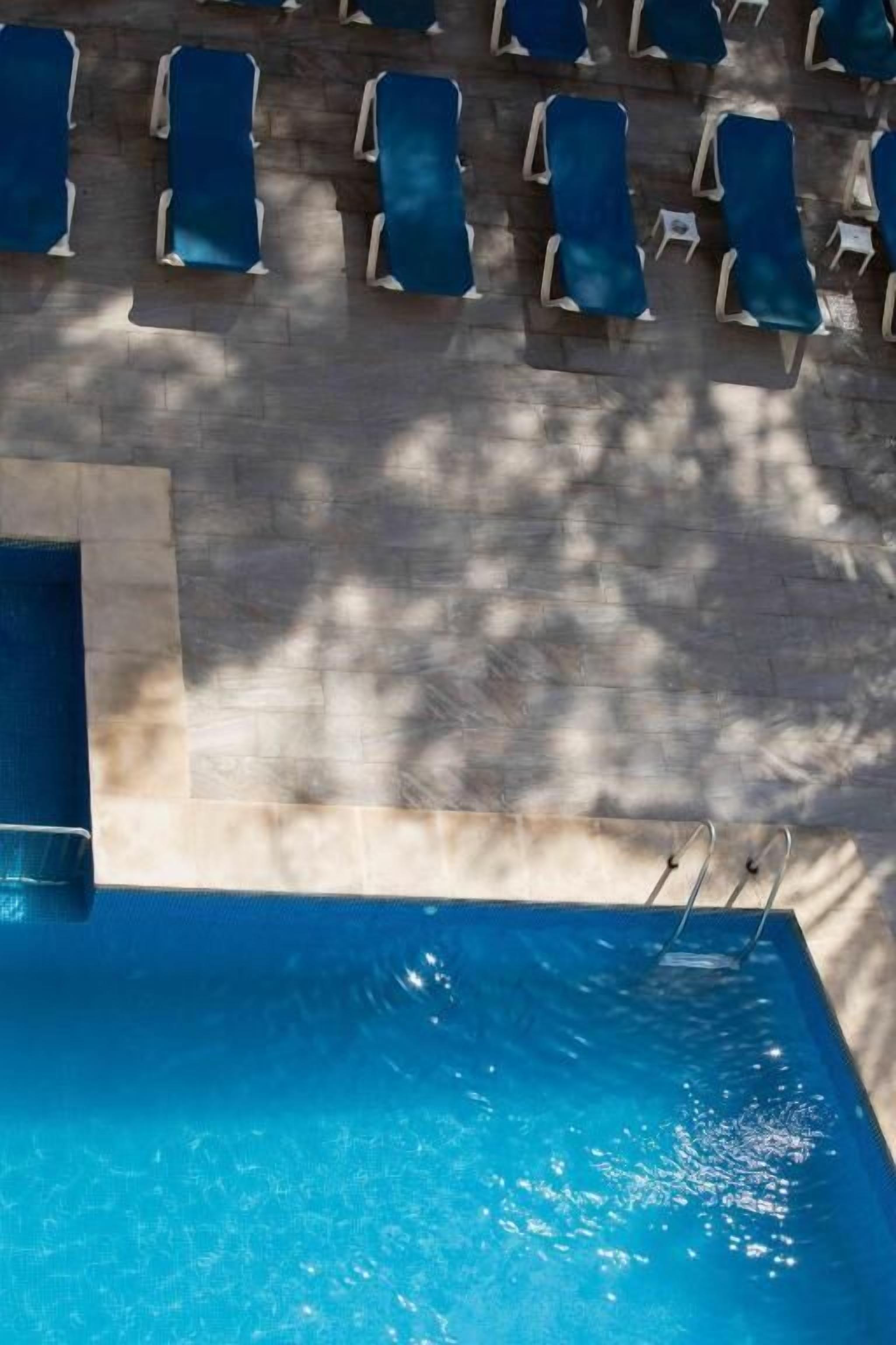 A swimming pool with sun loungers and a small table, surrounded by a tiled deck.
