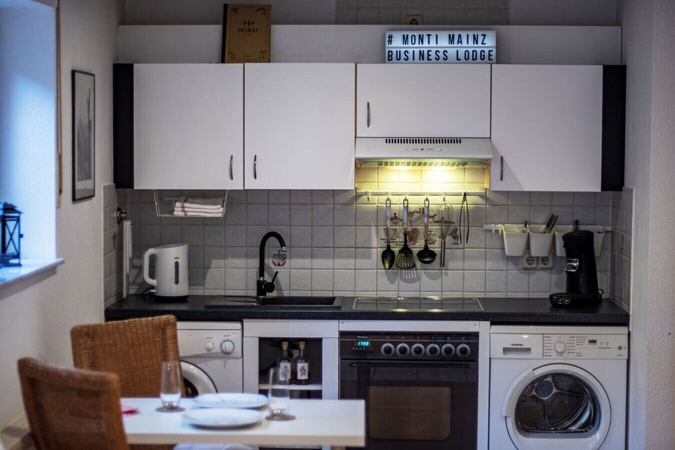 Een koelkast, een oven, een kookplaat, kookgerei, borden en bestek