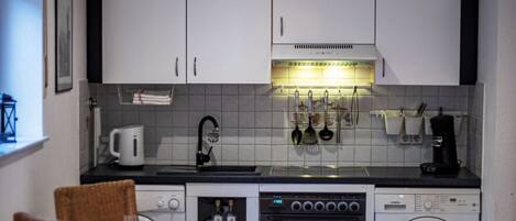 Een koelkast, een oven, een kookplaat, kookgerei, borden en bestek