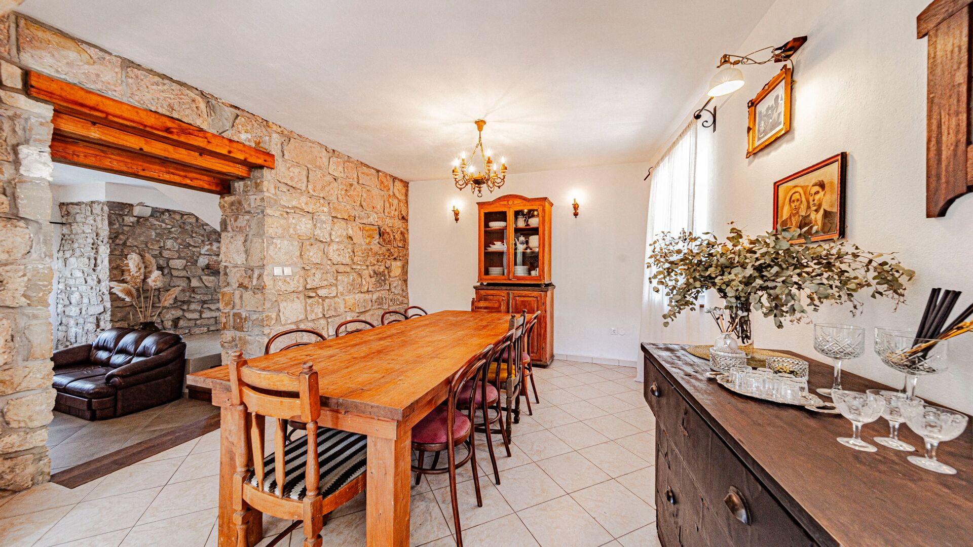 A dining area with a wooden table and chairs, a stone wall, a leather sofa, and a cabinet with glass doors.