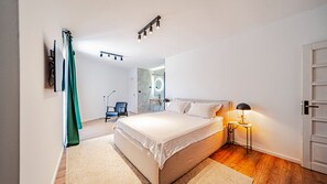 Un dormitorio moderno con una cama grande, un escritorio, una silla y un baño visible a través de una puerta abierta.