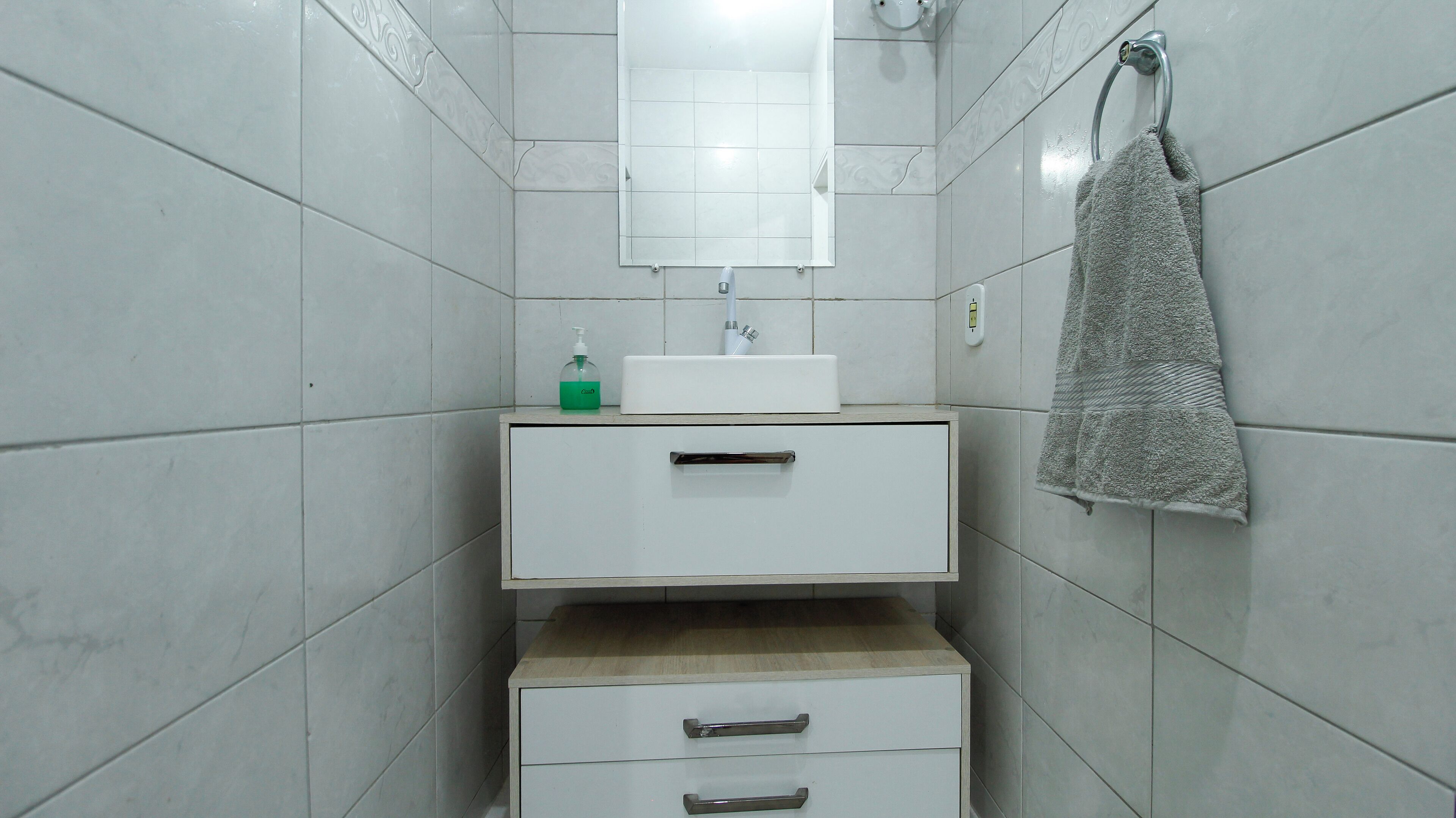A small, clean bathroom with white tiles, a mirror, a sink, and a towel rack.