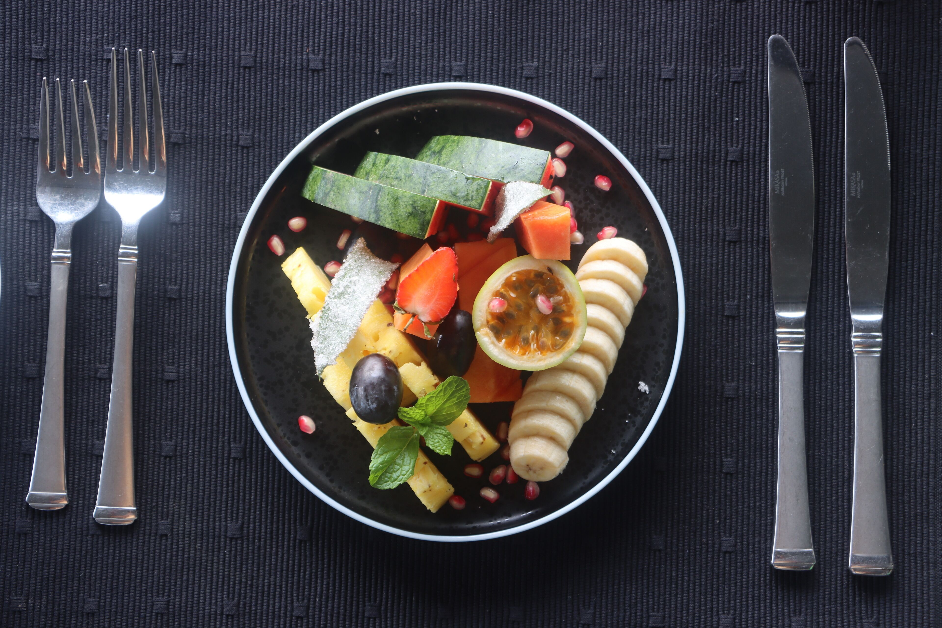 Een bord met verschillende soorten fruit en groenten op een donkere placemat.