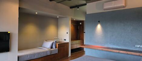 A modern hotel room with a large bed, a seating area with a bench, a ceiling fan, and an air conditioning unit.