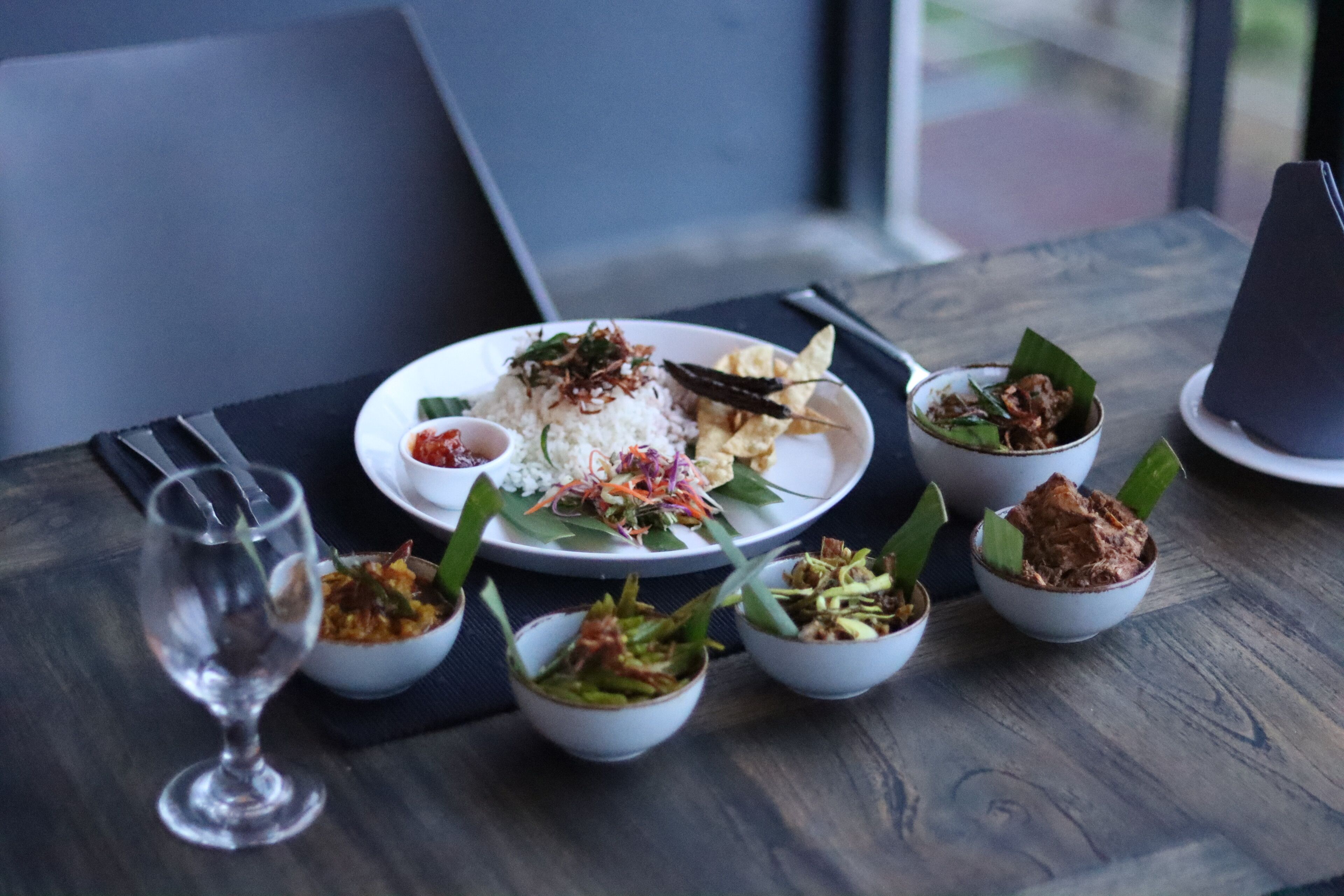 A dining table with a plate of food, including rice, vegetables, and a small bowl of sauce.