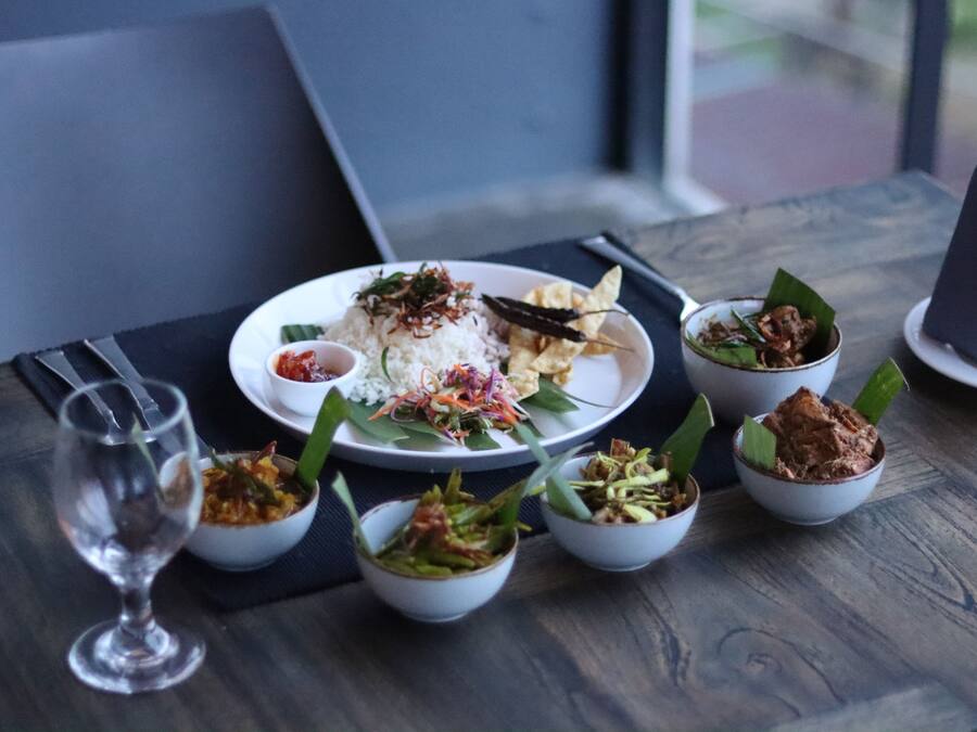 Una mesa de comedor con un plato de comida, que incluye arroz, verduras y un recipiente pequeño con salsa.