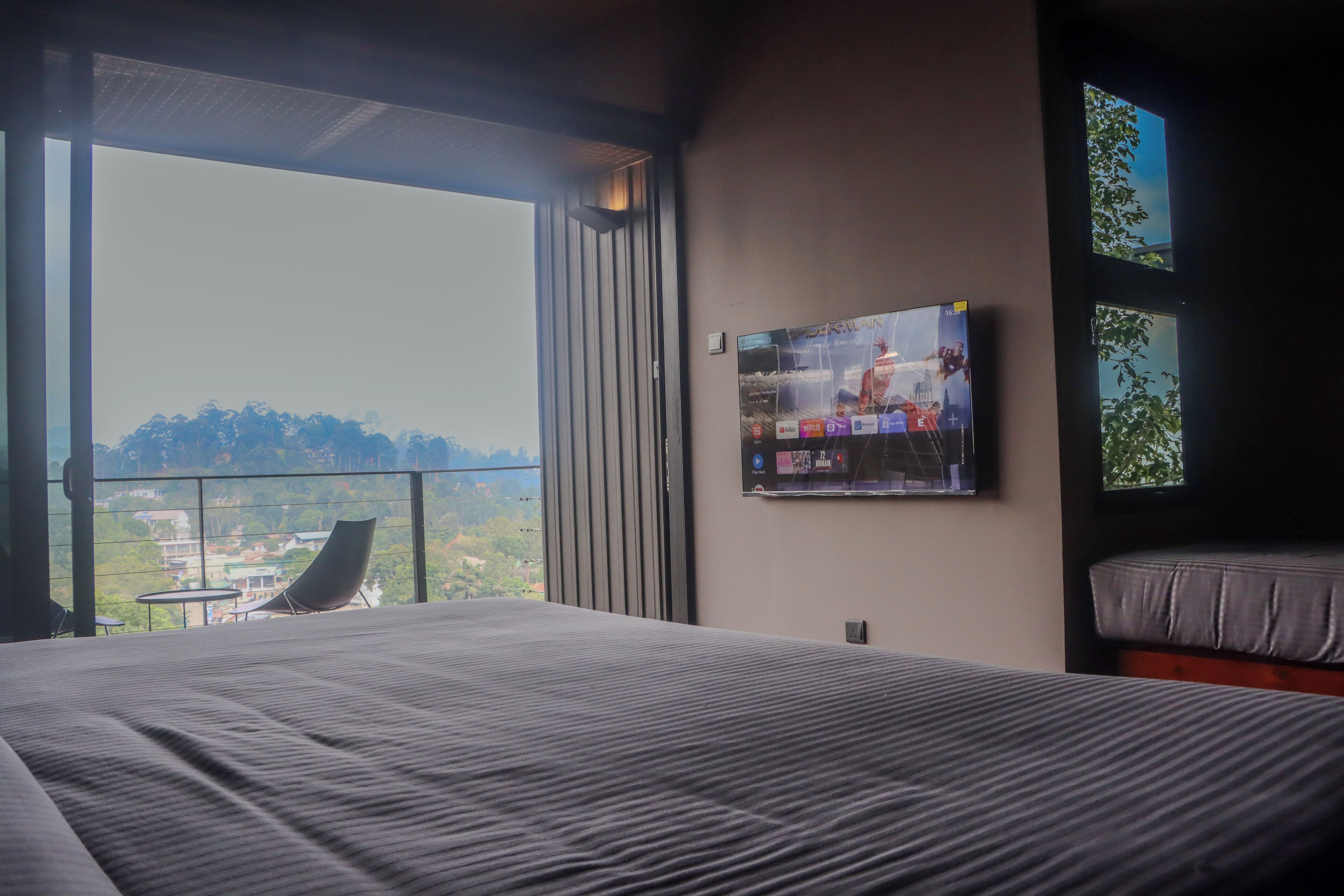 Quarto de hotel com uma cama grande, televisão na parede e varanda com vista para a cidade.