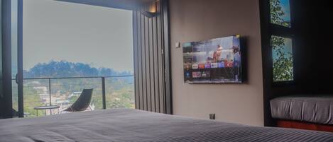 Habitación de hotel con una cama grande, un televisor montado en la pared y un balcón con vistas a la ciudad.