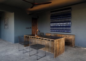 Un área de bar moderna con barra de madera, sillas de metal y una vitrina mural para botellas.