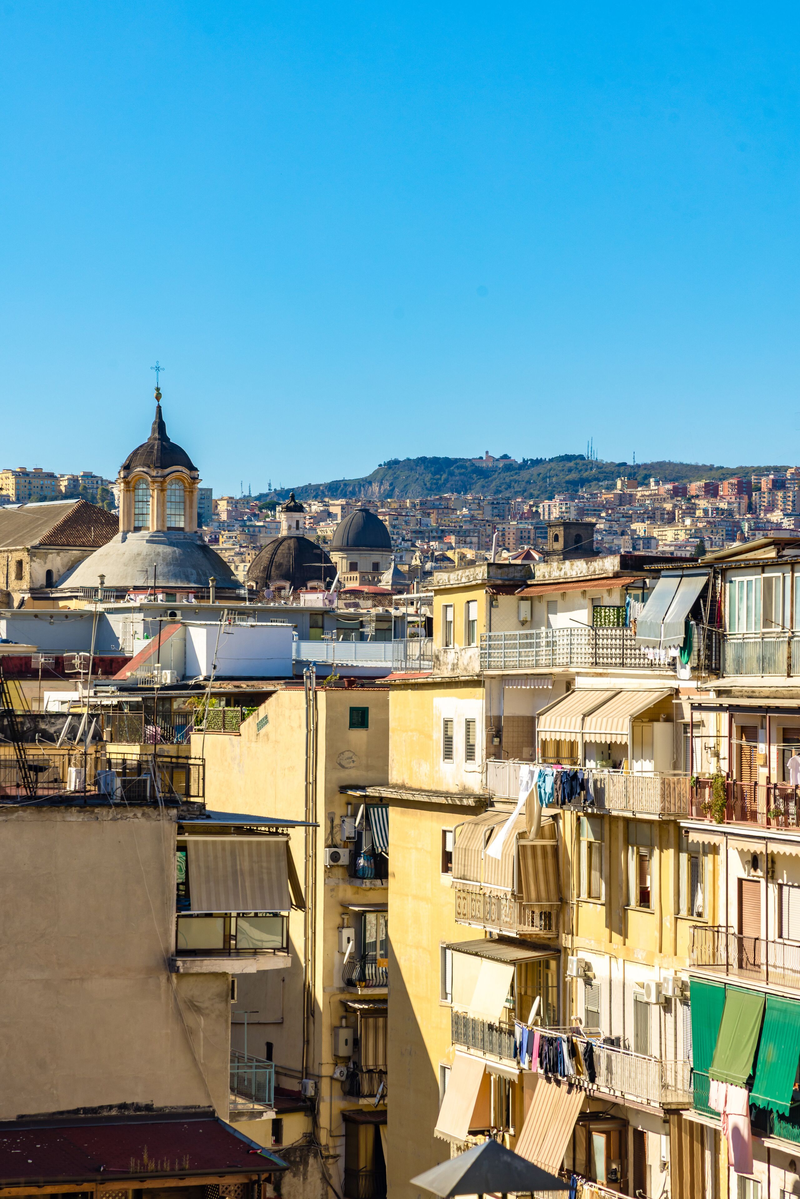 A densely packed urban area with multi-story buildings, balconies, and a prominent dome structure in the background.