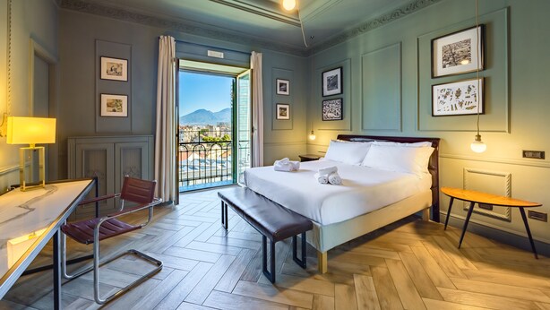 Une chambre d’hôtel équipée d’un lit, d’un bureau, d’une chaise, d’un banc et offrant une vue sur l’extérieur.