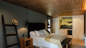 A modern bedroom with a wooden ceiling, a bed with white bedding, a bedside table, a bench, and a small kitchenette area. - Lun Lodges (Chacras de Coria)