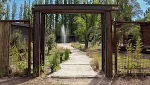 A pathway leading to a fountain, surrounded by greenery and metal fencing. - Lun Lodges (Chacras de Coria)