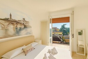 A hotel room with a bed, a painting of a bridge, a balcony with a view of buildings, and a chair. - VivimiHome - Oasi Verona con Garage (Verona)