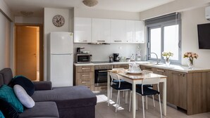 A modern kitchen with white cabinets, a microwave, and a dining area with a table and chairs. - Placebo Apartment in Greece (Volos)