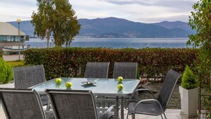 Un patio con mesa y sillas de vidrio, con vistas a un cuerpo de agua y montañas.