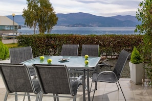 A patio with a glass table and chairs, overlooking a body of water and mountains. - Placebo Apartment in Greece (Volos)