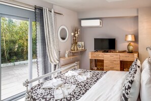 A bedroom with a large bed, a TV, a dresser, and a window with a view of greenery.