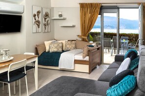 A modern living room with a sofa, a dining table with chairs, a TV, artwork on the wall, and a view of the outdoors.