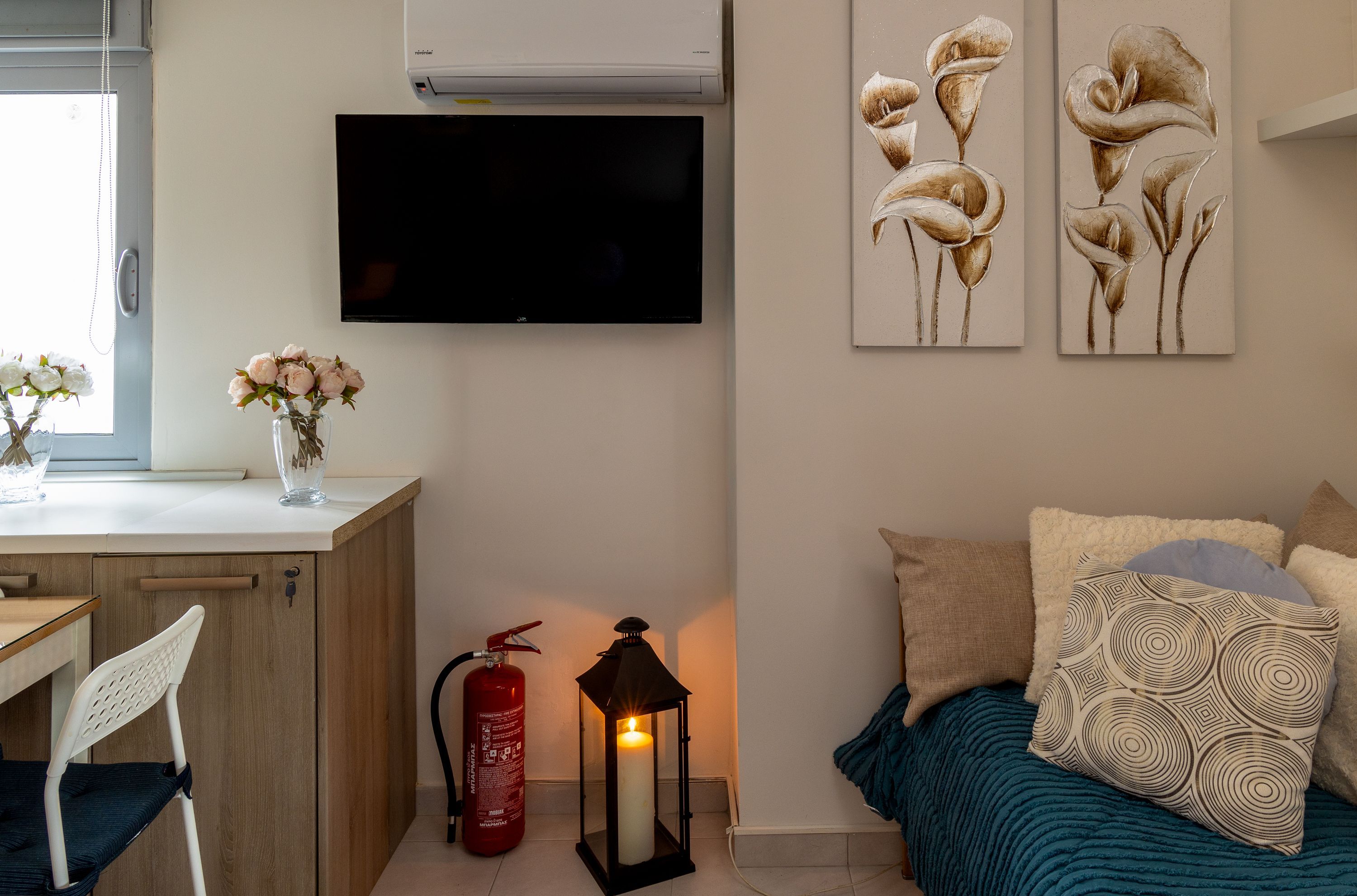 A bedroom with a bed, pillows, a TV, a fire extinguisher, a lantern, and artwork on the wall.