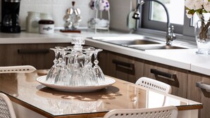 Una cocina con una mesa de vidrio, sillas blancas, un lavabo y un florero con flores.