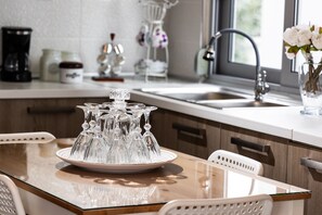 A kitchen with a glass-top table, white chairs, a sink, and a vase with flowers. - Placebo Apartment in Greece (Volos)