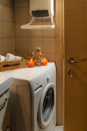 A front-loading washing machine with a control panel, a wooden drying rack, and three lit candles on top. - Placebo Apartment in Greece (Volos)