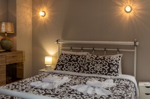 A neatly made bed with patterned bedding, a bedside lamp, and a wall-mounted light fixture. - Placebo Apartment in Greece (Volos)