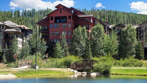 A large red building with multiple floors and balconies, surrounded by trees and a lake. - Founders Pointe 4649 Ski Mountain Condo Resort Amenities Walk to Ski Lifts (Winter Park)