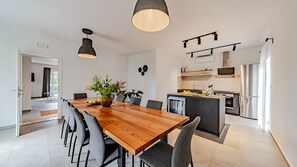 Eine moderne Küche mit einer zentralen Kochinsel, einem Essbereich mit Holztisch und Stühlen sowie Blick auf den angrenzenden Wohnraum.
