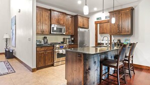 Una cocina moderna con armarios de madera, electrodomésticos de acero inoxidable y una isla central con taburetes de bar.