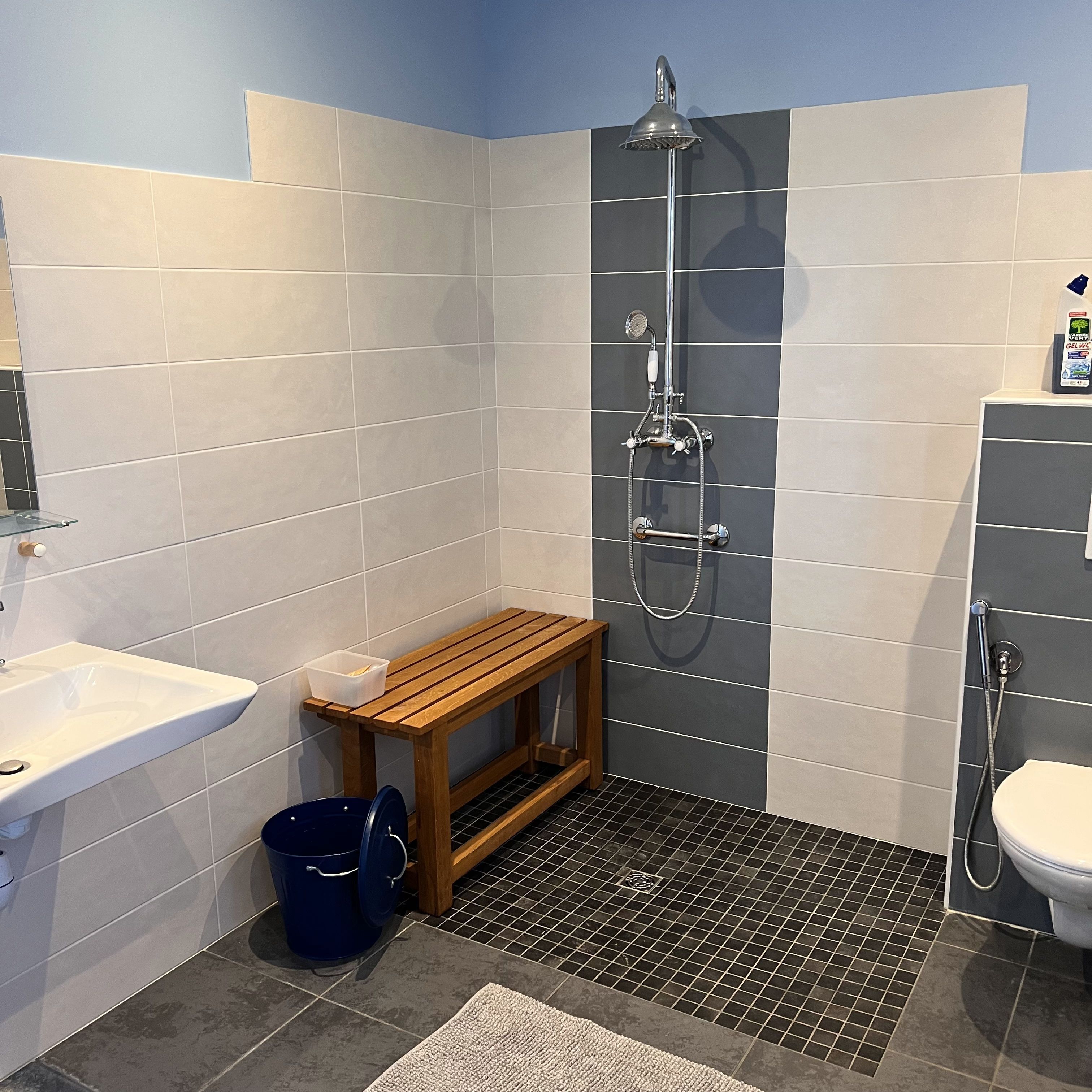 A bathroom with a shower, toilet, sink, and a small wooden bench.